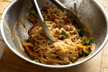 A view of an Asian noodle dish in a large metal mixing bowl.