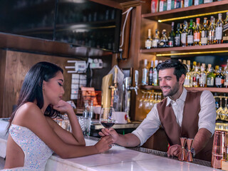 Bartender giving glass of wine to woman customer at bar counter .