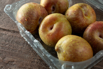 A view of several speckled plumcots in a plastic container.