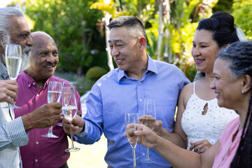 In garden, senior diverse friends toasting champagne, sharing conversation at wedding