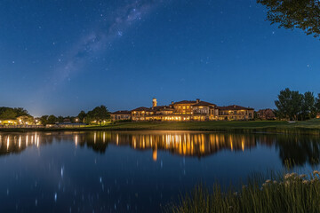 Obraz premium A serene lakeside estate at night, with a multi-story Italianate-style mansion and a tall clock tower in the distance.