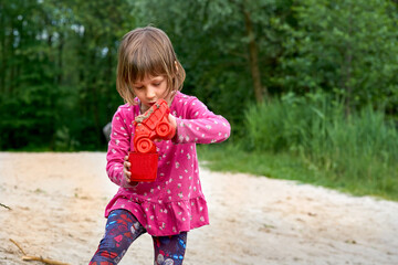 Little girl in red dress playing with toys on sand on nature