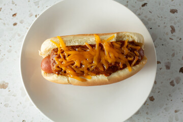 A top down view of a chili cheese dog on a plate.