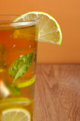 A close-up of a glass of a ice tea with lime and lemon slices in it. The drink is served in a glass with slice of lemon on the side. Warm orange background. Focus on slice of lemon