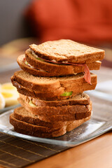 A photo of stacked breakfast sandwiches made with cucumber, cheese, and salami on whole wheat bread, with defocused boiled eggs in the background