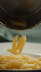vertical shot penne rigate falling on white plate