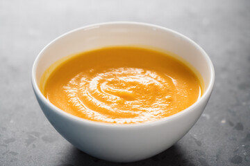 Pumpkin spicy soup puree in white bowl on concrete background