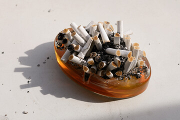 A closeup photo of numerous cigarette butts in an orange ashtray placed on a white table, highlighting texture and details