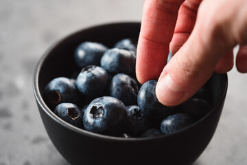 Man hand pick ripe blueberries from black bowl on concrete background closeup