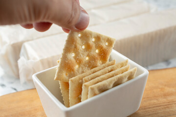 A view of a hand pulling up a saltine cracker from a condiment cup.