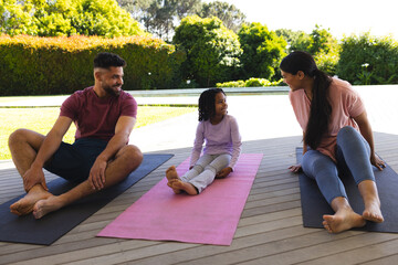 Family enjoying outdoor yoga session on mats, bonding and smiling together