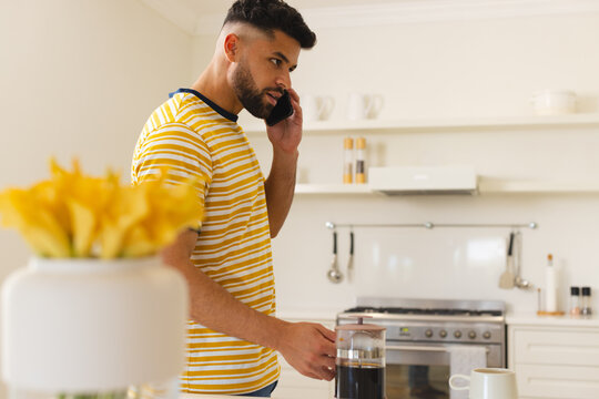 In kitchen, man talking on smartphone while making coffee, looking focused
