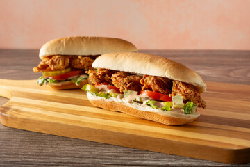 A view of some po boy sandwiches, on a wood board.