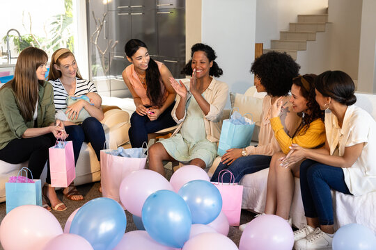 Diverse female friends celebrating baby shower at home, surrounded by balloons and gifts, smiling