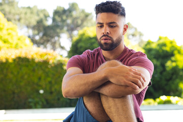Young man sitting outdoors, deep in thought, enjoying peaceful garden surroundings