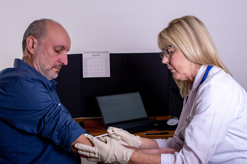 Vaccination a patient gets an injection, jab at a GP Doctor's appointment surgery He roll's up a shirt sleeve for the clinician to administer the treatment using a syringe and needle.