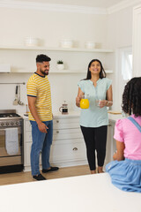 Smiling woman pouring orange juice in kitchen while family enjoys morning together