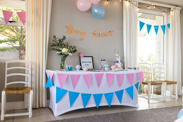 Baby shower decorations with pink and blue banners and cupcakes on table, at home