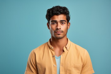 A man with a beard and a yellow shirt is standing in front of a blue wall