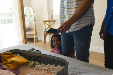 Child hugging parent while packing suitcase at home, smiling with joy