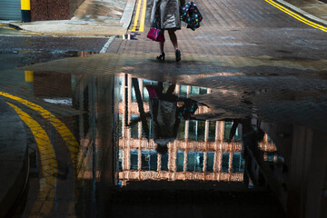 Blurred refelction of woman with trench coat and umbrella on rain puddle