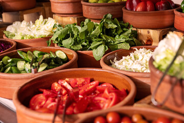 Delicious buffet table with Fresh and Vibrant Organic Vegetables in Rustic Clay Bowls and greens, featuring variety of healthy and colorful plant-based dishes for vegetarian or vegan meal