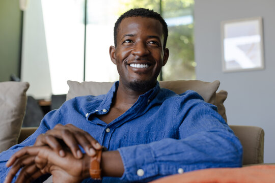 Smiling man in blue shirt relaxing on couch at home, enjoying leisure time