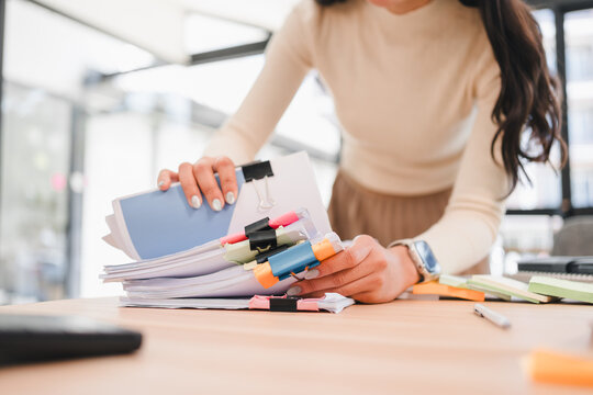 Asian businesswoman organizing colorful documents on desk in modern office, showcasing productivity and focus.