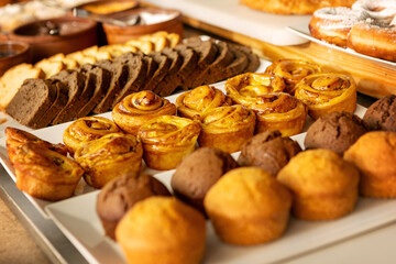 Close-up variety of freshly baked pastries, muffins and sweet rolls displayed on buffet table in...