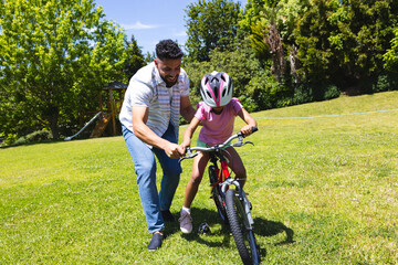 Fototapeta premium Father teaching daughter to ride bicycle in park, enjoying sunny day together