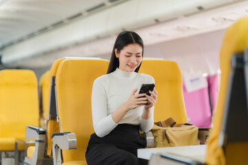 Connected in Transit: An Asian woman sits comfortably on an airplane, engrossed in her phone,...