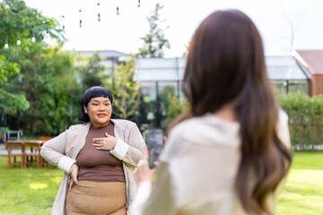 Fototapeta premium Happy beautiful Asian millennial woman friends enjoy and fun celebration reunion meeting using mobile phone taking picture together at dinner party in the garden at restaurant on holiday vacation.