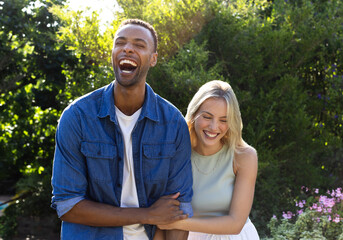 Diverse couple laughing joyfully in sunny garden, enjoying outdoor celebration together