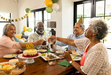 diverse senior friends celebrating 60th birthday with cake and drinks at home