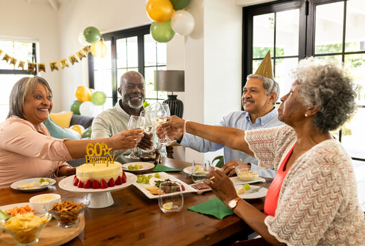 diverse senior friends celebrating 60th birthday with cake and drinks at home