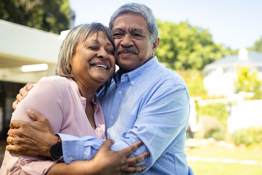 Happy senior diverse senior couple embracing in garden, enjoying sunny day in garden, copy space