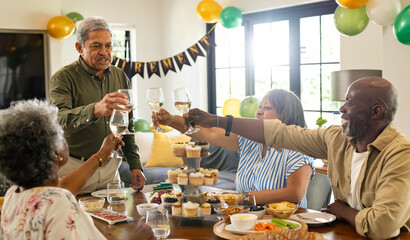 Group of senior friends toasting with wine glasses at home during party celebration