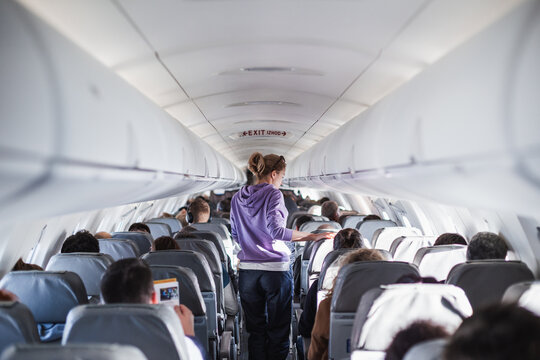 Interior of airplane with passengers on seats and female traveler walking the aisle. Commercial economy flight service concept