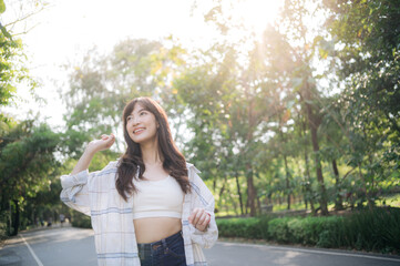 Asian woman enjoying summer outdoors, breathing fresh air in park with sunlight filtering through...