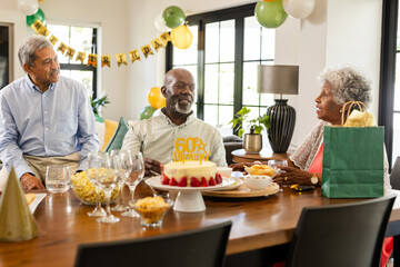 Celebrating 60th birthday, senior diverse friends enjoying cake and conversation at home