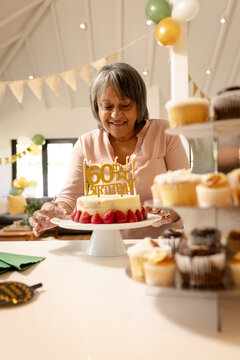 Senior woman celebrating 60th birthday with cake and cupcakes at home
