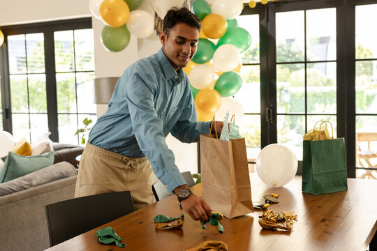 Man preparing gift bags on table with balloons for party celebration at home