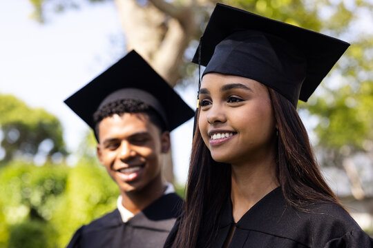 Graduation day, diverse students in caps and gowns smiling in garden