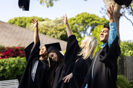 Diverse graduates joyfully throwing caps in air, celebrating success in garden together