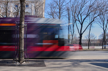 A colorful tram rushes down a lively street lined with trees under a bright blue sky, showcasing...