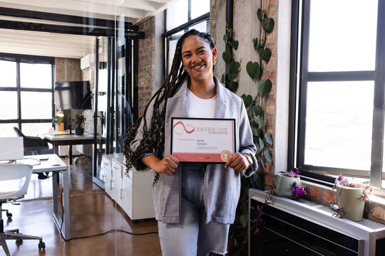 Proud woman holding achievement certificate in modern office, smiling confidently