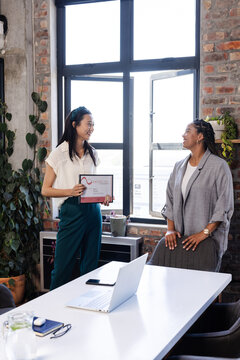 Asian woman holding certificate smiling with colleague in modern office