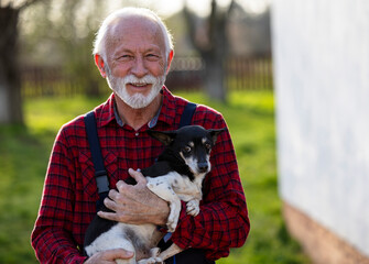 Elderly man smiling while holding cute dog in arms in backyard