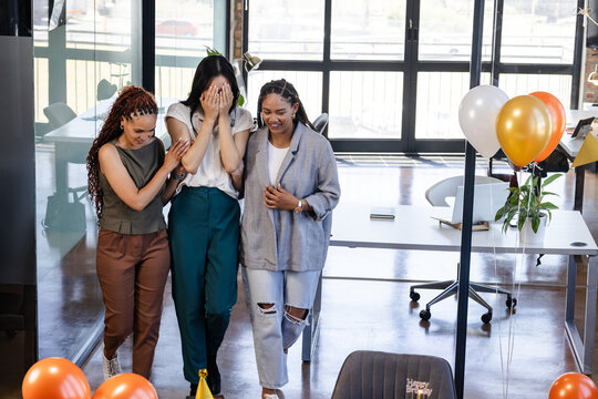 Female diverse colleagues celebrating surprise party in modern office with balloons and laughter