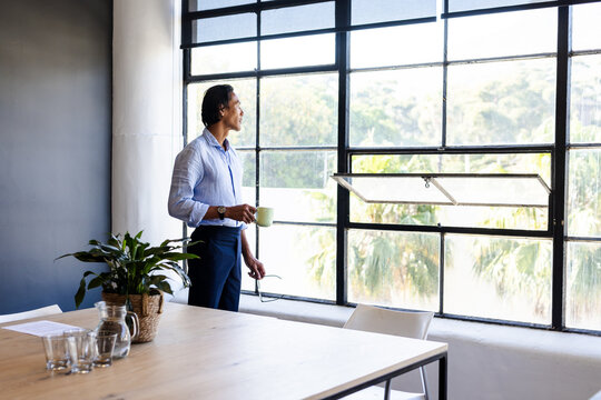Businessman holding coffee cup, gazing out office window, contemplating ideas, copy space